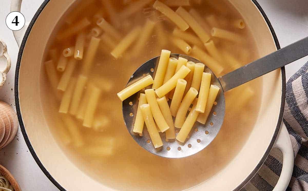 Cooked ziti in a slotted spoon over the pan.