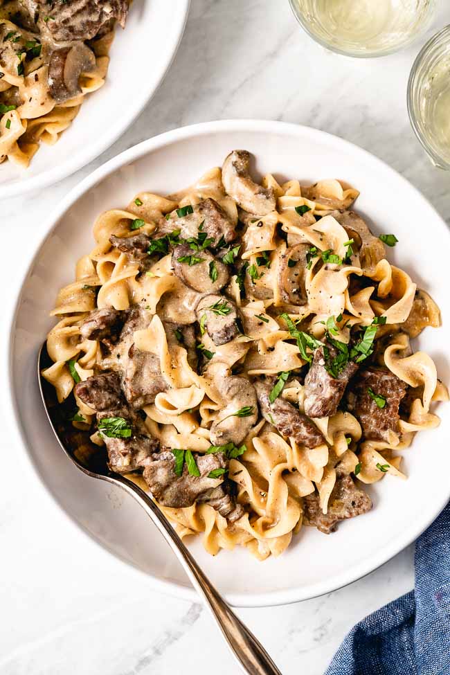 A bowl of homemade easy beef stroganoff is garnished with fresh herbs and photographed from the top view. - Foolproof Living