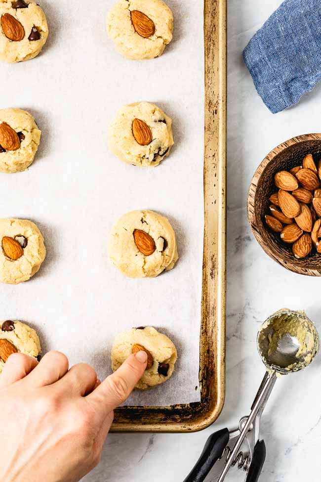 paleo chocolate chip cookies made with almond flour are portioned on a cookie sheet and decorated with an almond photographed from the top view.