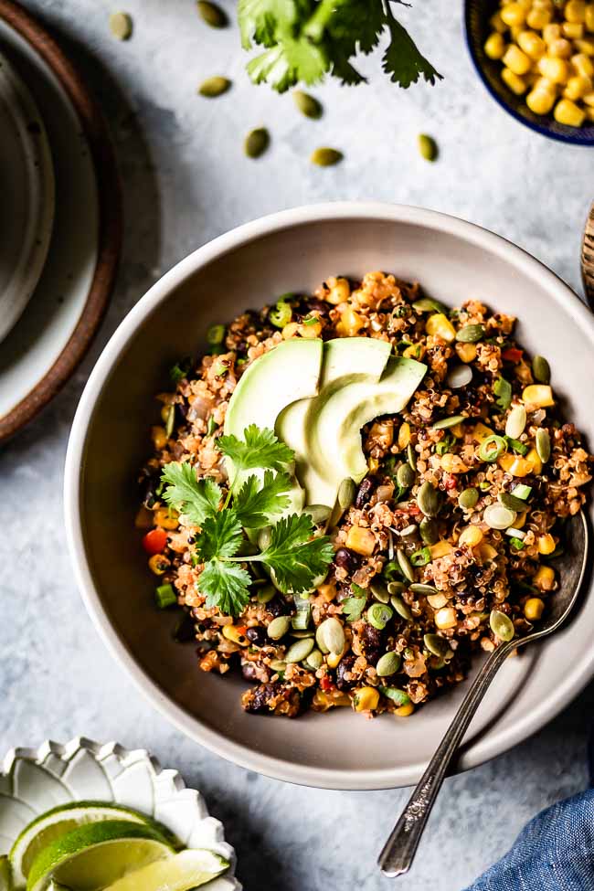 A big bowl of weeknight Mexican quinoa is garnished with avocados, pumpkin seeds, and cilantro and photographed from the top view.