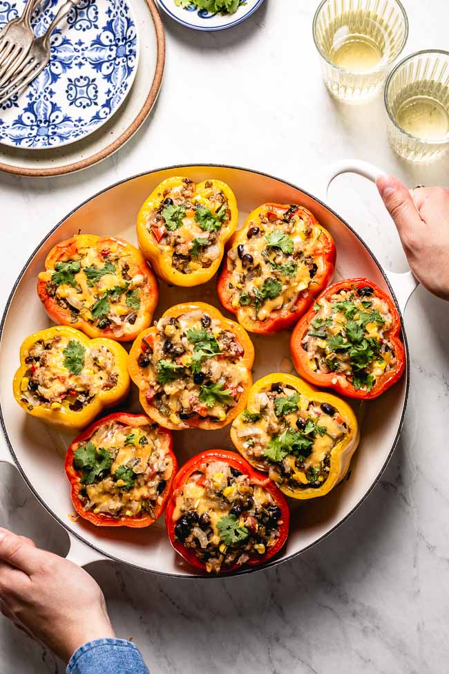 A woman is serving a big pot of Mexican Stuffed Peppers photographed from the top view.