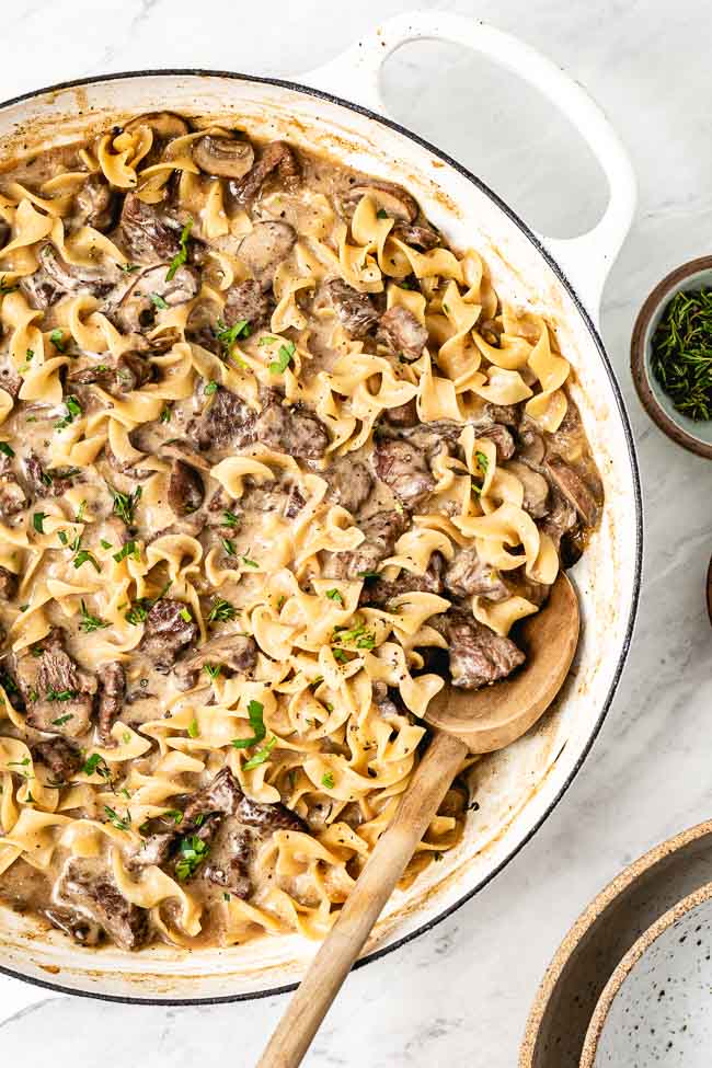 Skillet Beef Stroganoff is photographed from the top view from a close up distance with fresh herbs on top. It looks creamy and delicious. Foolproof Living