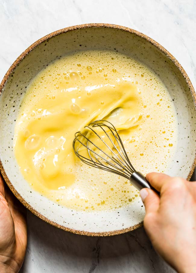 Wet ingredients are photographed from the top view while a woman is whisking them.