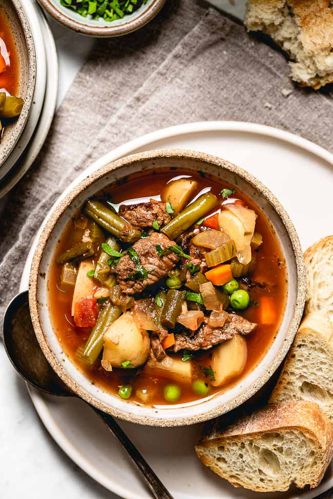 Crockpot Vegetable Beef Soup placed in a bowl and served with crusty bread photographed from the top view.