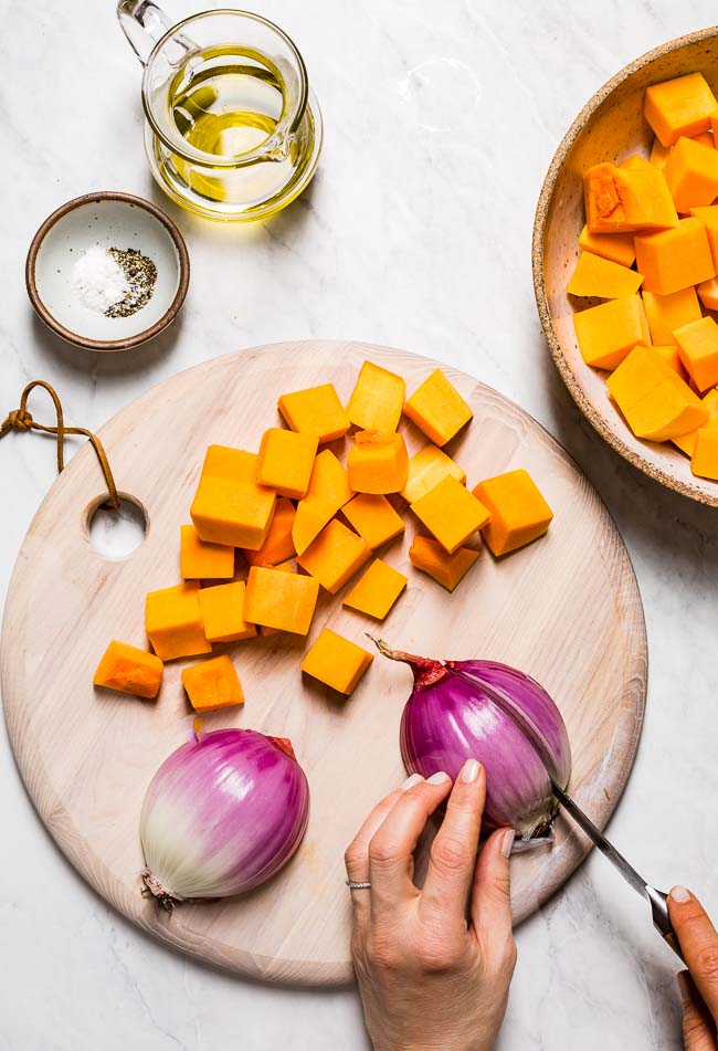 A woman is photographed as she is cutting the sweet potatoes and red onion