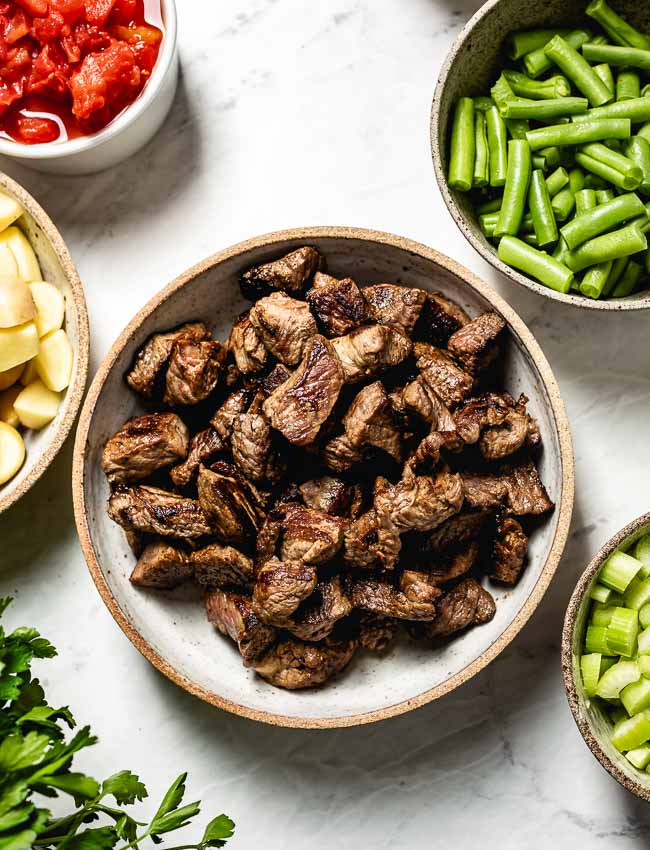 Browned beef is photographed along with fresh vegetables 