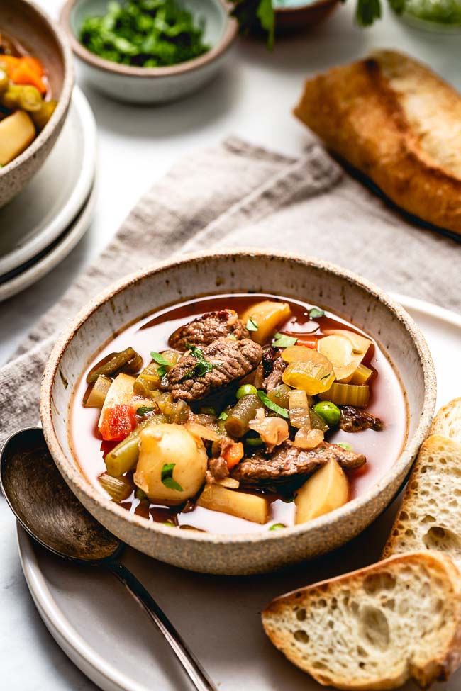 a bowl of Crockpot Vegetable Beef Soup is served with crusty bread and photographed from the front view.