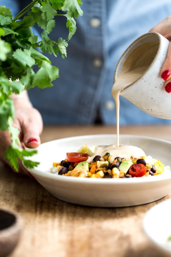 A woman is drizzling the bowl with sauce