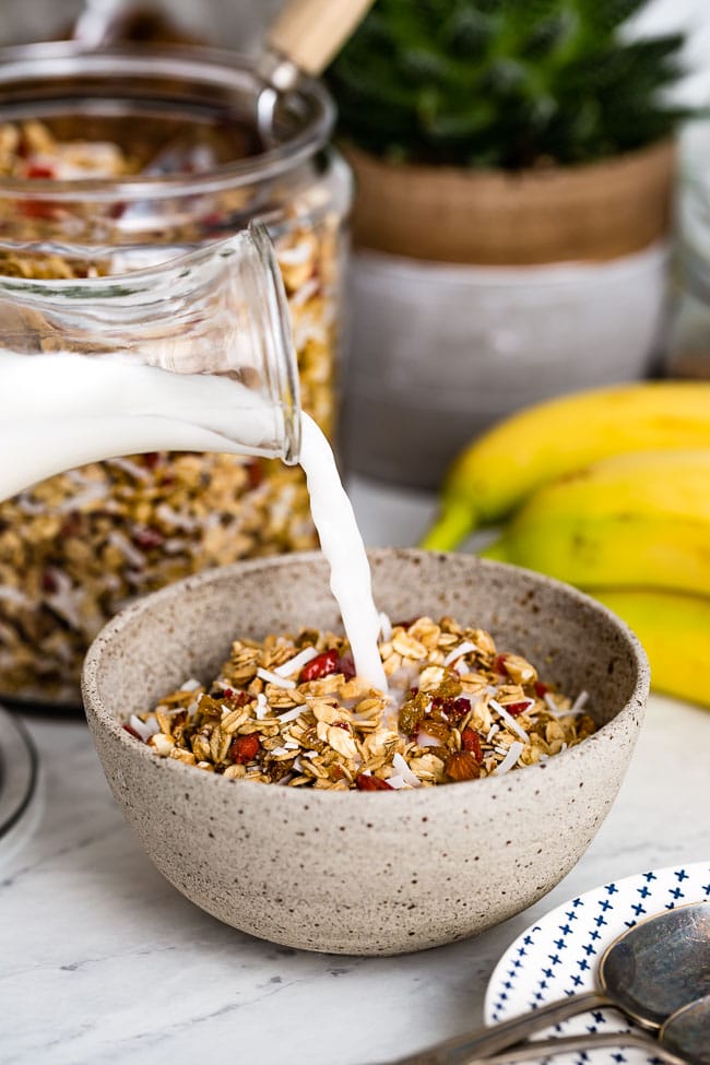 The Best Low Sugar Chunky Granola Recipe is placed in a bowl and photographed from the front view as it is being drizzled with milk