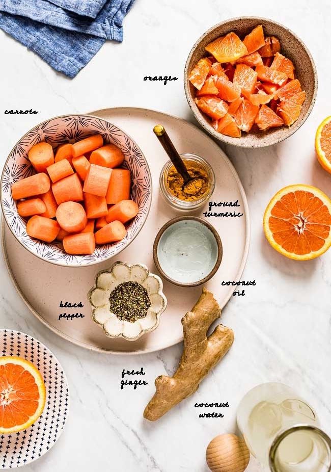 Ingredients for Orange Ginger Turmeric smoothie are photographed from the top view on a white marble backdrop.