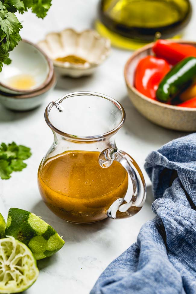 Chili Lime Vinaigrette placed in a small jug and photographed from the front view with some vegetables around it.