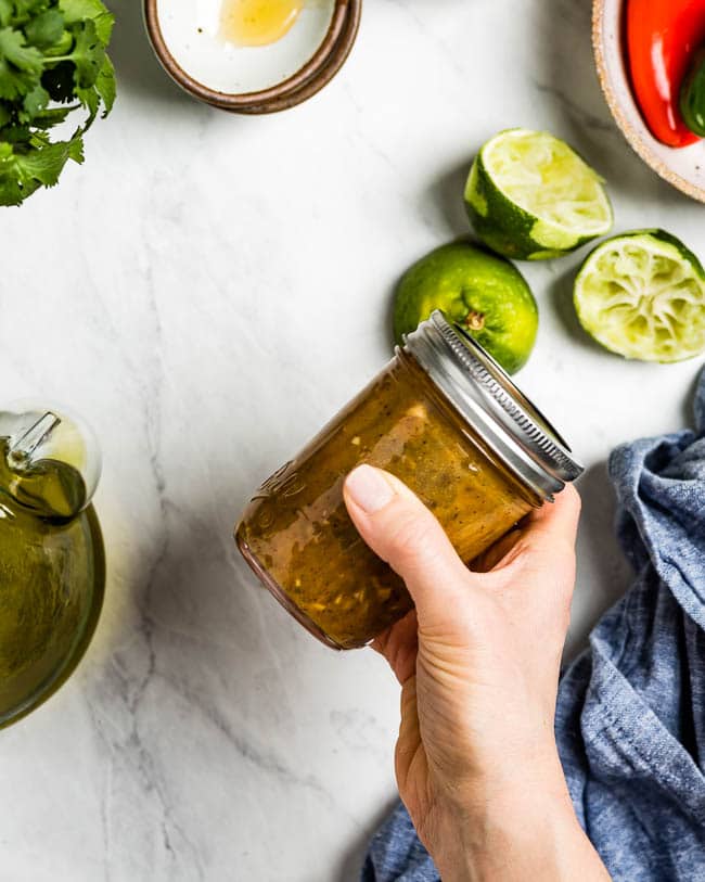A woman is photographed as she is shaking a mason jar with Chilli Lime Salad Dressing