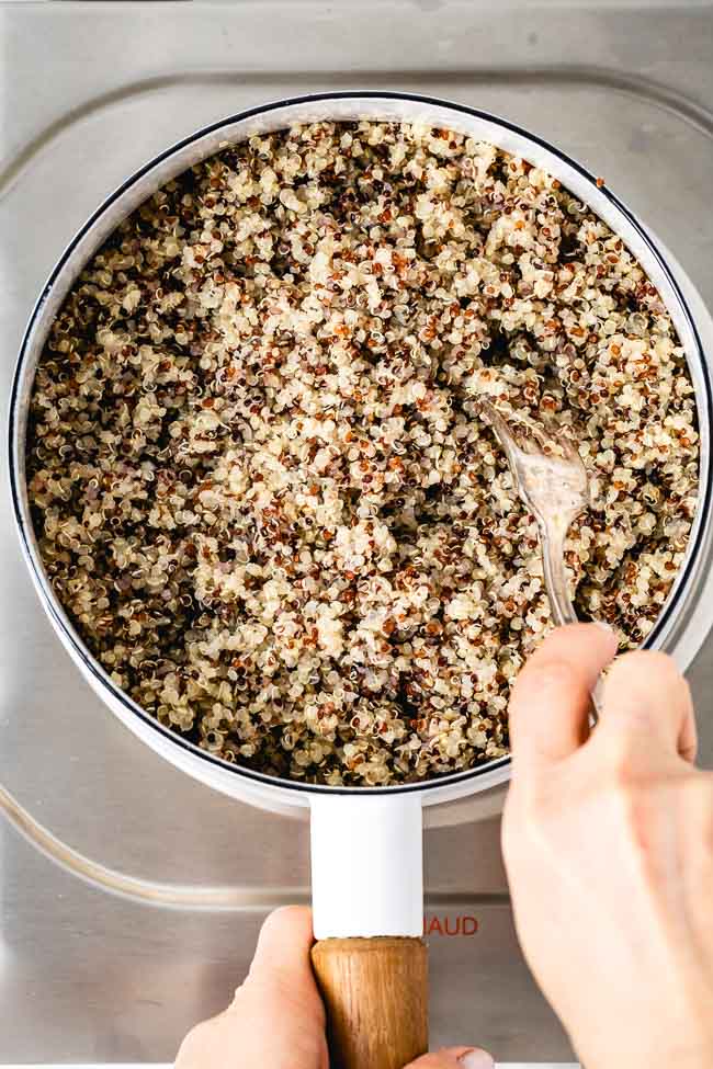 Cooked quinoa is being fluffed with a fork photographed from the top view