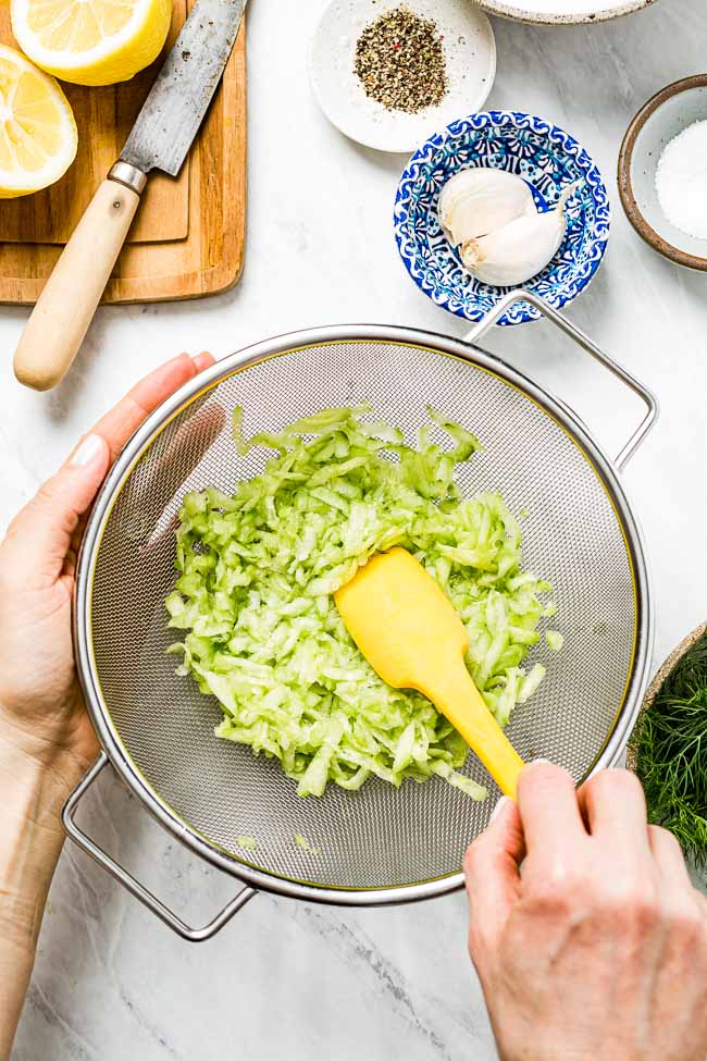 Shredded cucumber placed in a mesh sieve and is being drained by a woman