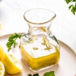 A bottle of salad dressing is in a jug with lemons on the side