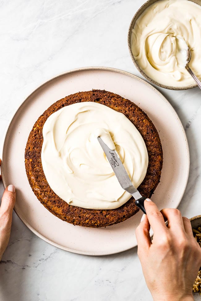 A woman is spreading carrot cake with maple cream frosting