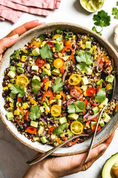 A big bowl of Southwestern Quinoa Salad is photographed from the top view as a woman is placing it on the table