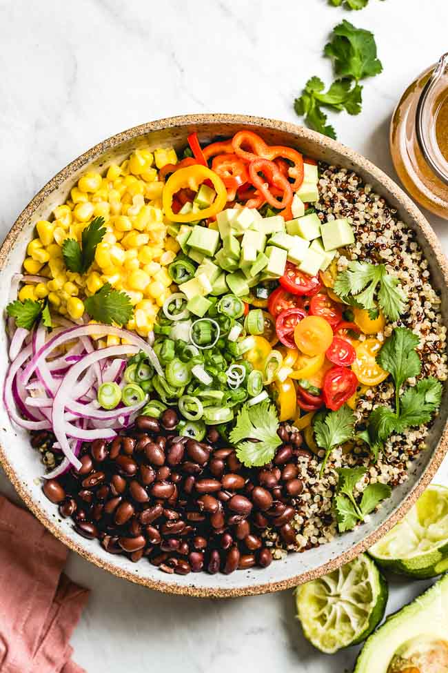 A big bowl of Southwestern Quinoa Salad with avocado is photographed from the top view with chili lime dressing on the side
