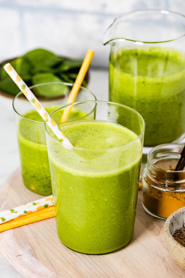 green turmeric smoothie in a glass with straws