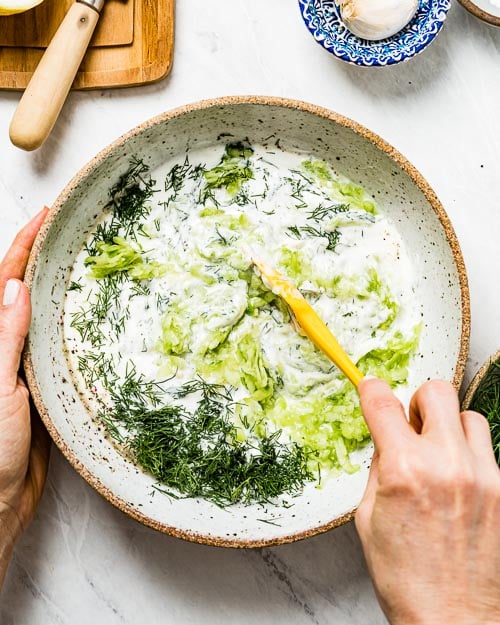 A woman is mixing Mediterranean yogurt sauce with dill