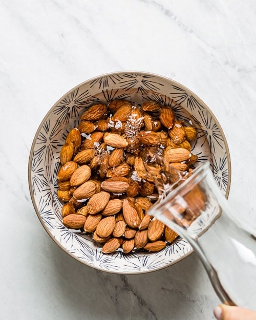 water is being poured into a bowl of almonds