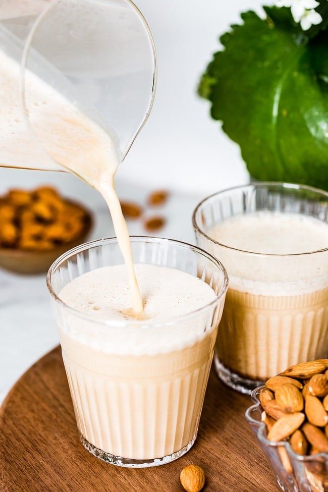 A glass of almond milk made from almond butter is being poured into a glass