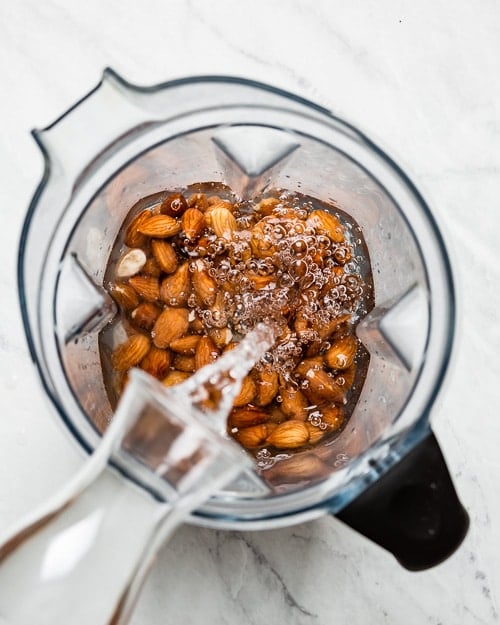 Water is being poured in a blender filled with almonds to make DIY homemade almond milk recipe