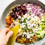 A woman is dressing a bowl of quinoa salad with feta