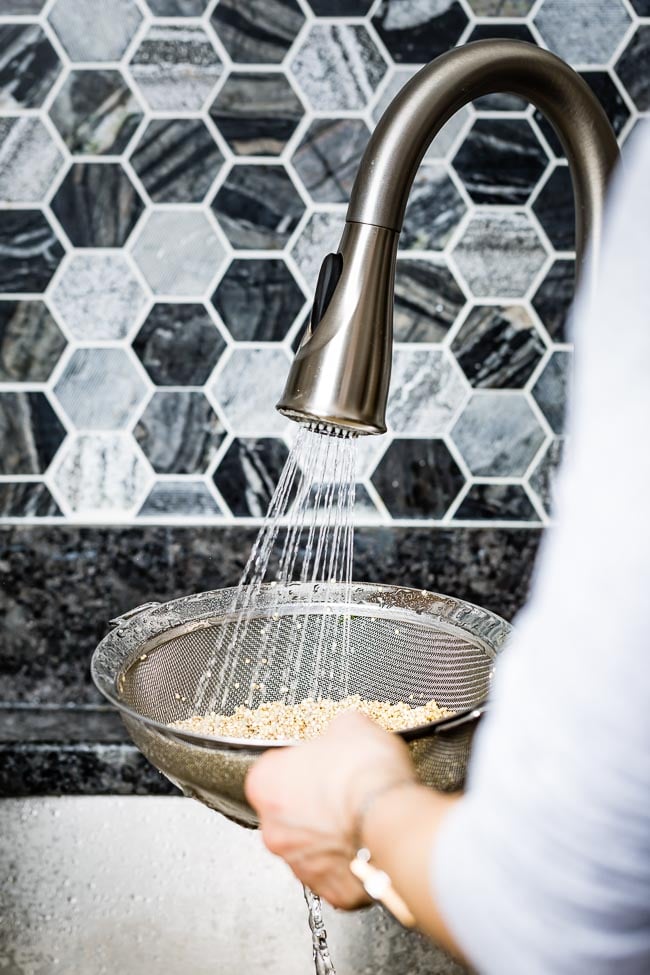 A woman is rinsing quinoa in a fine mesh strainer