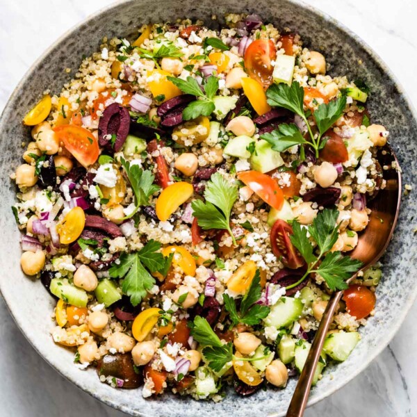 Overhead shot of mediterranean quinoa salad with chickpeas, feta, tomatoes, olives, and parsley in a bowl with a spoon.