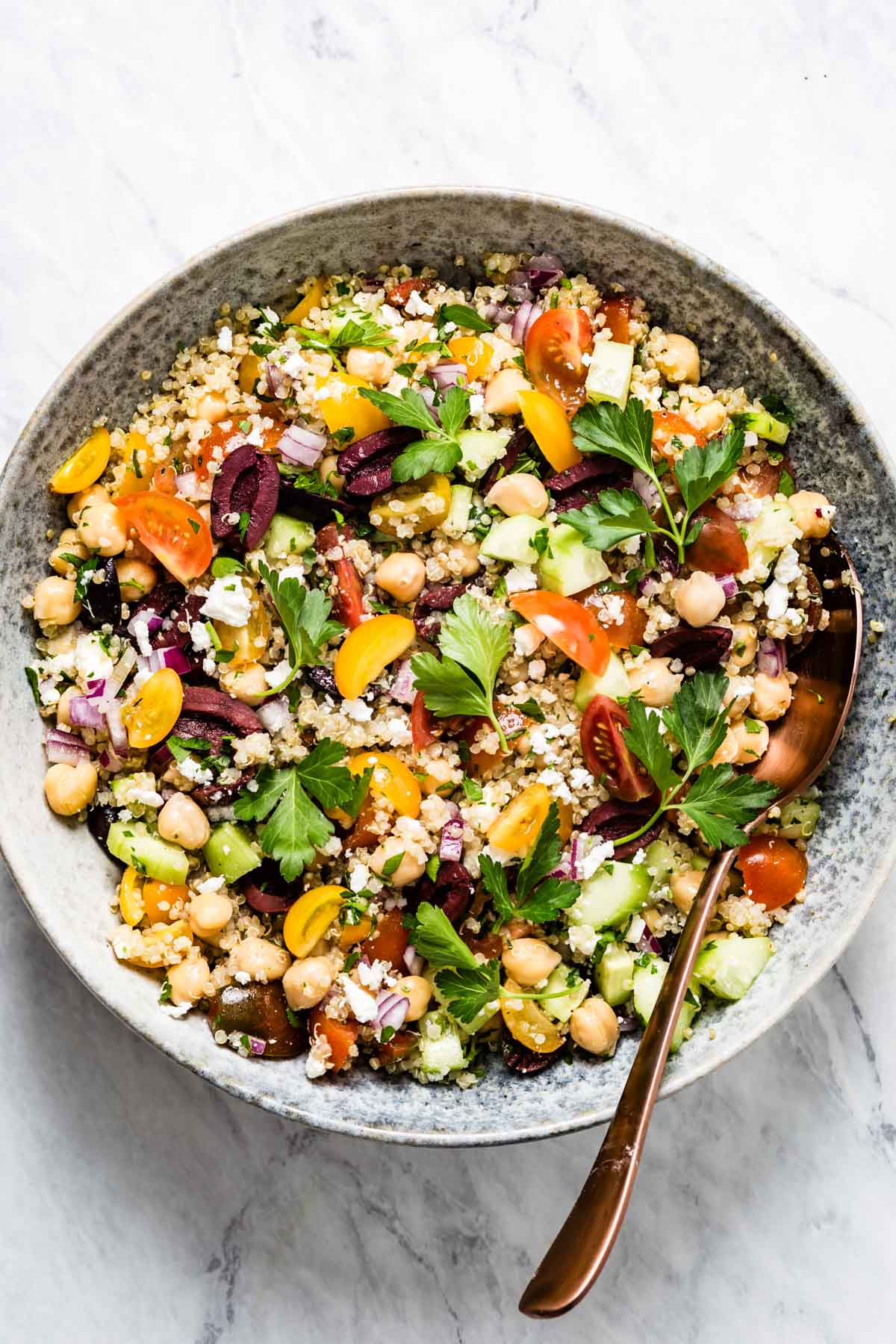 Overhead shot of mediterranean quinoa salad with chickpeas, feta, tomatoes, olives, and parsley in a bowl with a spoon.