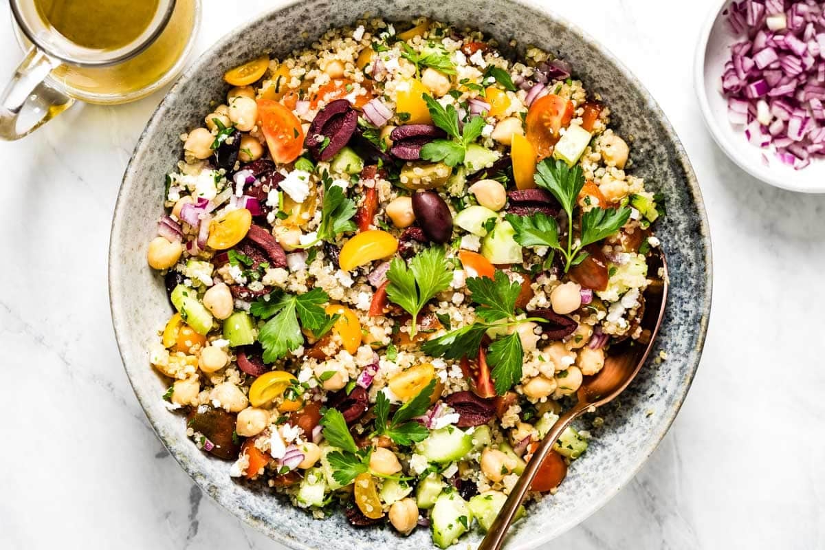 A bowl of Mediterranean quinoa salad from the top view with dressing and chopped onions on the side.