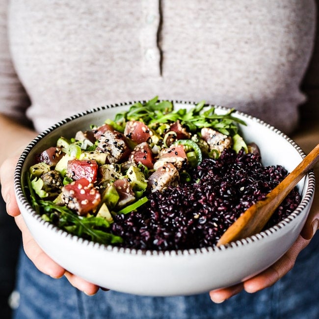 A woman is holding a bowl of Asian Ahi Tuna Salad recipe served in a bowl with black rice