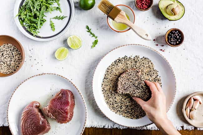 A woman is crusting tuna steaks with sesame seeds