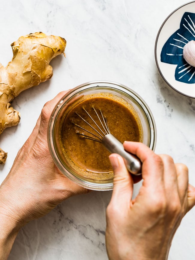 A woman is mixing sesame soy ginger vinaigrette in a jar with a whisk