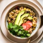 A bowl of Instant pot Mexican quinoa is garnished with avocado slices, pickled radishes, and cilantro