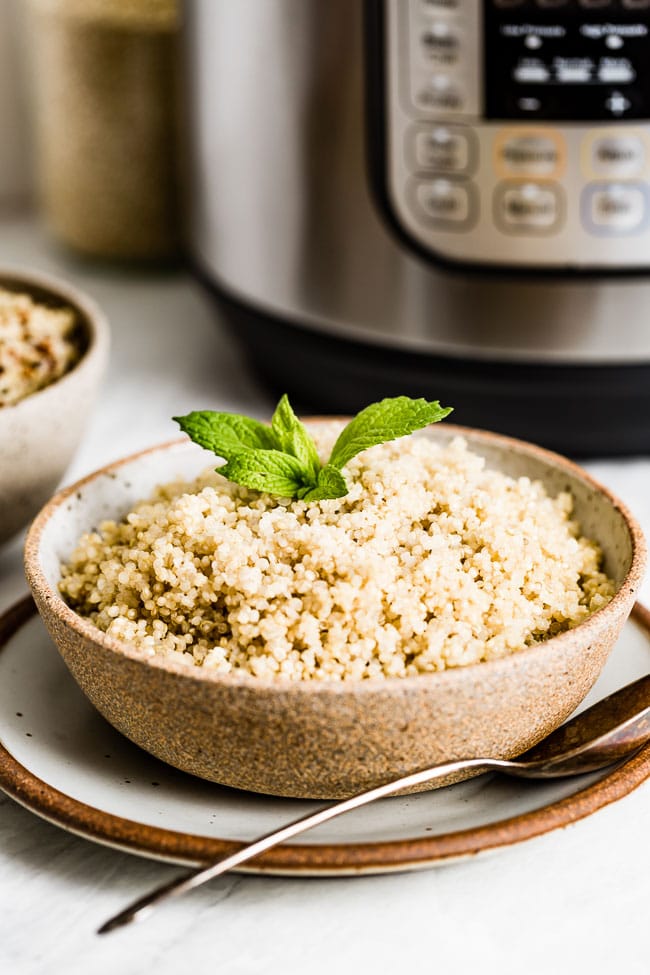 A bowl of quinoa cooked in a pressure cooker is in front of an instant pot