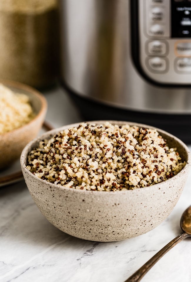 A bowl of tricolor quinoa in front of a pressure cooker