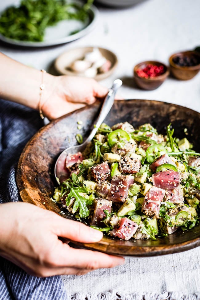 A woman is serving Asian Style Seared Tuna Salad in a wooden salad bowl