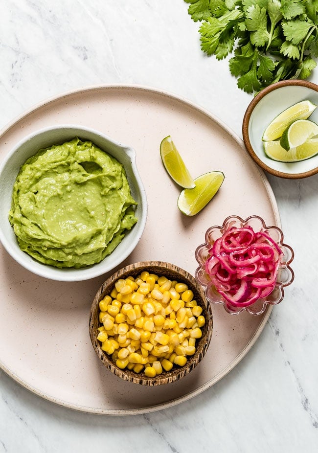 The topping options: Avocado crema, corn, pickled onions, and lime wedges