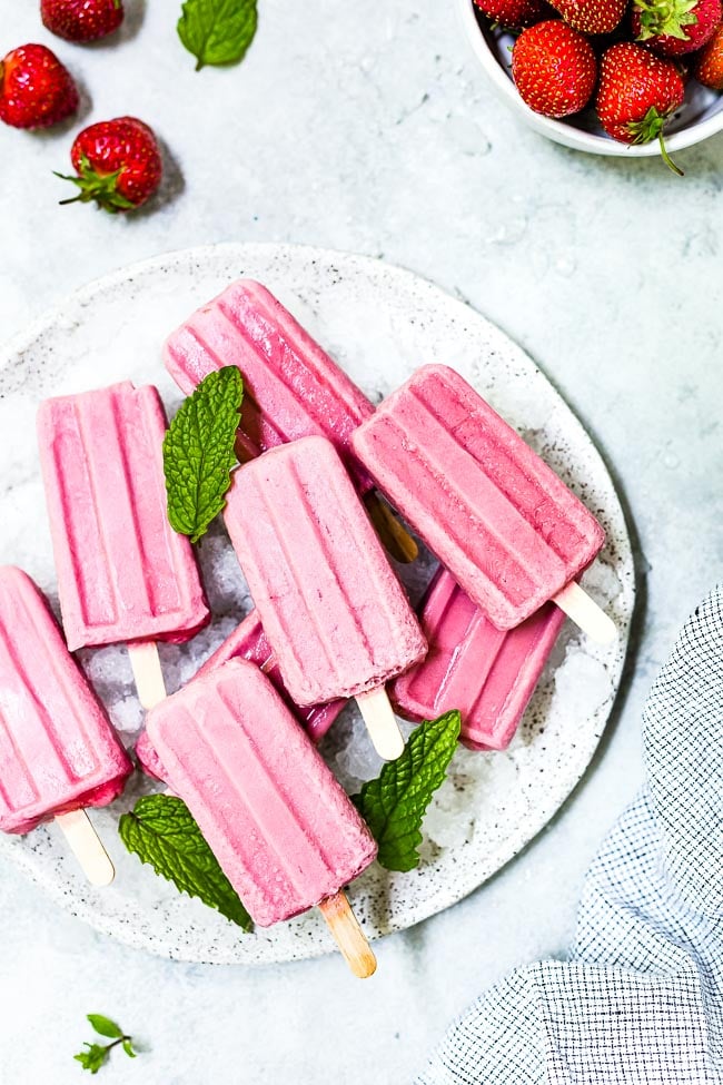 strawberry milk popsicles in a plate filled with ice.