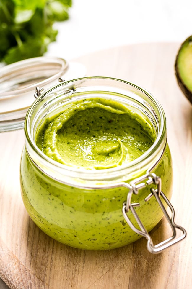 A jar of homemade avocado salad dressing with cilantro and a raw avocado on the side