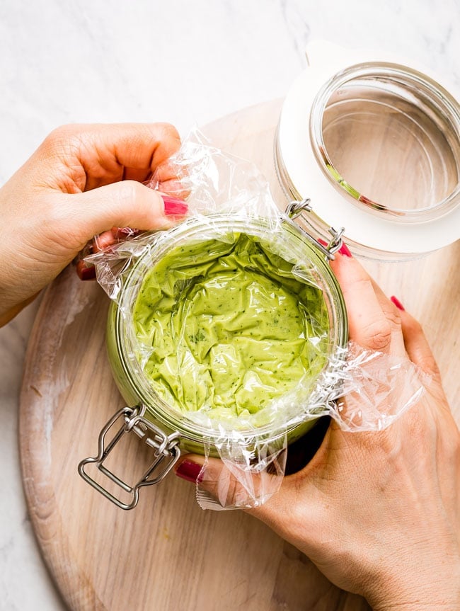 A woman is placing plastic wrap over the sauce to prevent it from turning brown