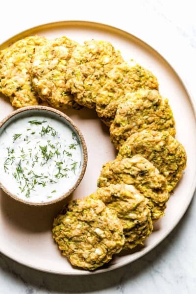 Baked Zucchini Fritters placed on a plate with a dipping sauce on the side