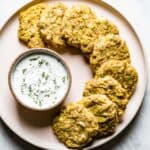 Baked Zucchini Fritters placed on a plate served with yogurt sauce on the side