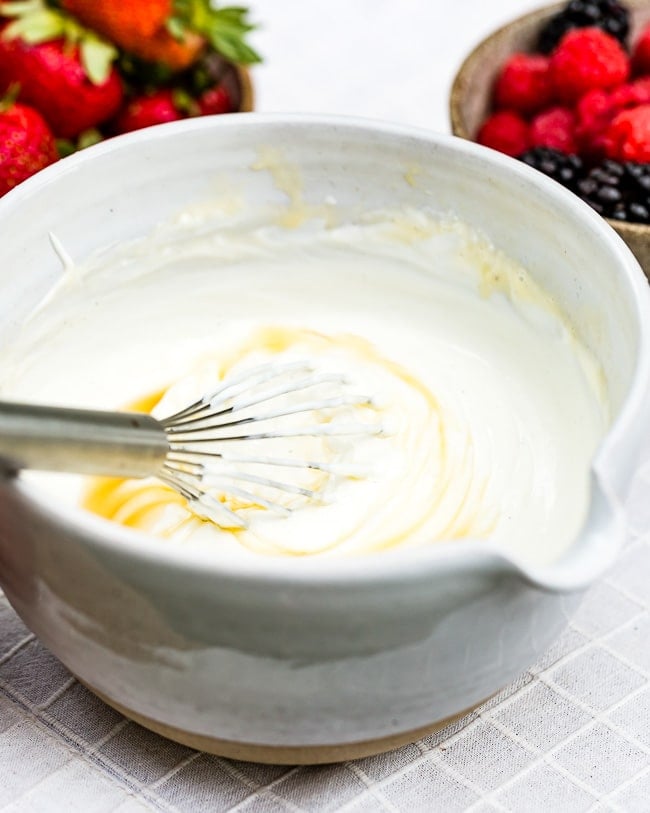 A bowl of fruit dip made with yogurt mixed with honey with a whisk in the bowl.
