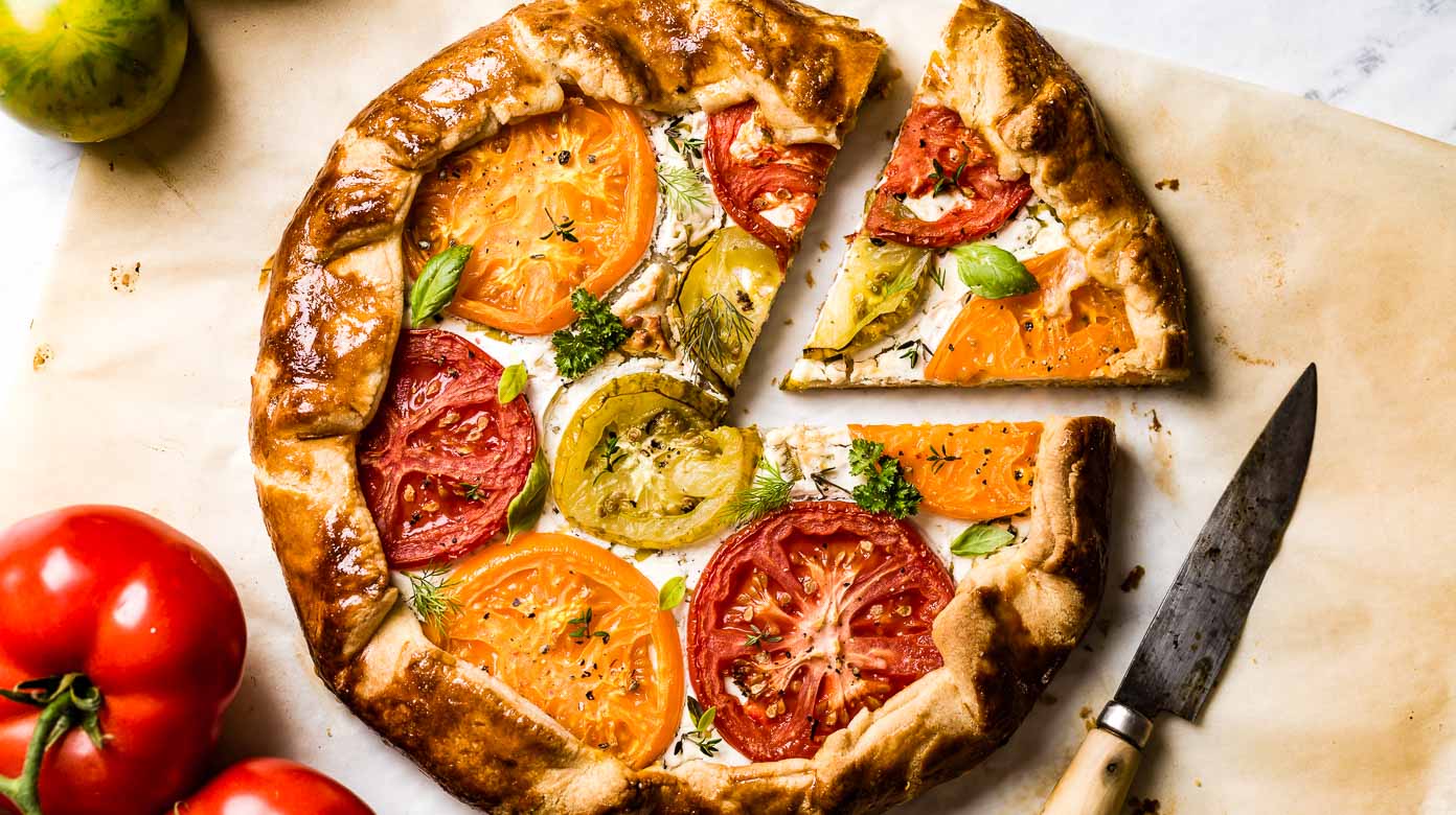 Premium Photo  Homemade galette or savory pie with red and yellow tomatoes  and basil on old newspaper or parchment paper. top view.