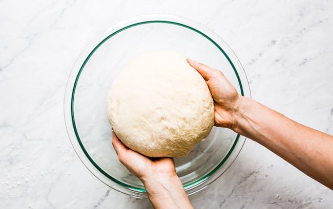 A woman is placing the dough in a lightly oiled bowl