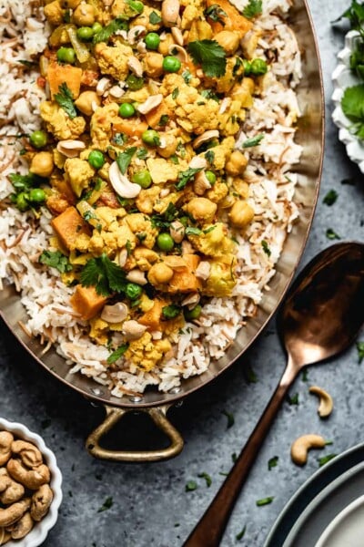 Cauliflower Curry with coconut milk and sweet potatoes placed in a copper pot garnished with cilantro and cashews from the top view