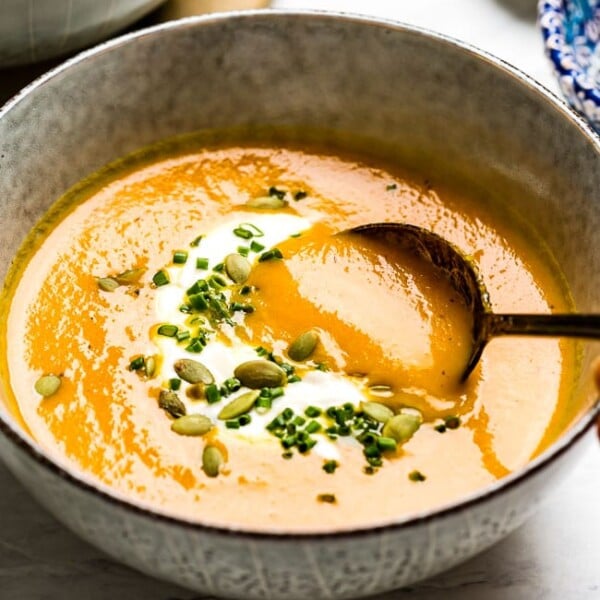 Carrot Ginger Soup garnished with creme fraiche and chives in a bowl with a spoon